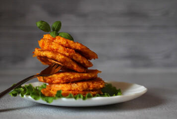 natural dietary carrot pancakes on a plate with lettuce leaves and a fork on a gray background
