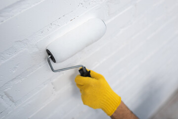 Cropped view of man in glove painting brick wall at home