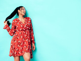 Young beautiful smiling female in trendy summer red dress clothes. Sexy carefree woman posing near blue wall in studio. Positive model having fun and going crazy. Cheerful and happy
