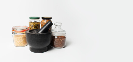 Close-up of granite stone grinder bowl of black near jars with some spices, on white background with copy space. Panoramic banner.