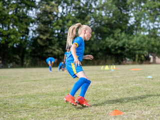Girl (8-9) dressed in uniform practicing on soccer field © Cultura Creative
