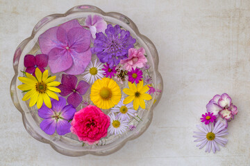 Fototapeta na wymiar Runde alte Glasschale mit sommerlichen Blüten in gelb und rosa
