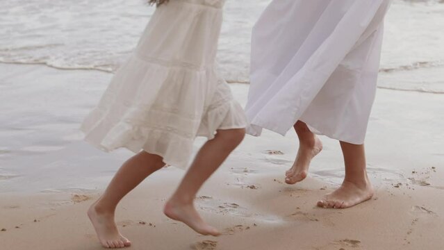 A young mother dances with her daughter on the golden sand of the beach. Mother and daughter are happy.