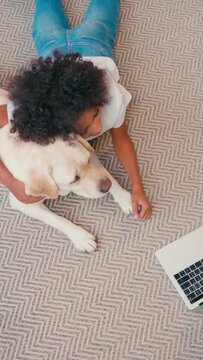vertical view of african american girl hugging dog while lying on carpet at home