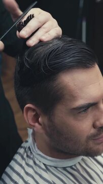 vertical video of barber cutting hair of brunette man