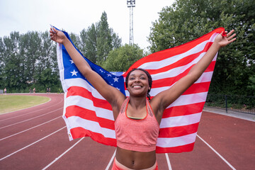 Portrait of smiling athletic woman with American flag on running track