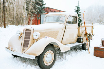 beige retro pickup truck decorated for Christmas and New Year with vintage interior items, suitcases, skis, sledge, blankets, Christmas ornaments, winter time