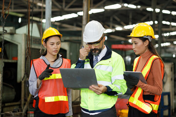 Team maintenance engineers men and women inspect relay protection system with laptop systems. They work a heavy industry manufacturing factory.