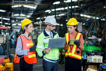 Team maintenance engineers men and women inspect relay protection system with laptop systems. They work a heavy industry manufacturing factory.