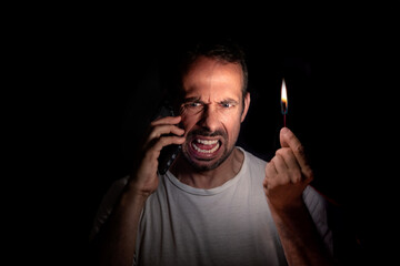 Angry man talking on the phone with a match in the dark. Blackout concept. Selective focus.