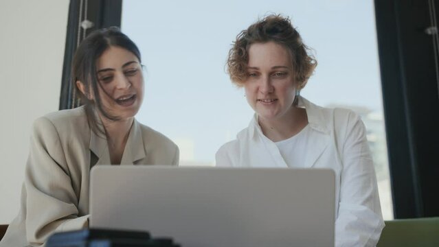 Two young women using laptop in professional photo studio, watching photo, video. Model and photographer discussing result of work. Creative team choosing shots after photo session