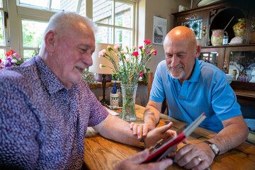 Senior male couple using tablet at home - obrazy, fototapety, plakaty