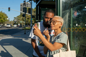 Couple waiting at bus stop and woman applying lip gloss