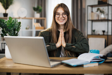 Fototapeta na wymiar Smiling caucasian woman in casual wear sitting on workplace on yoga pose relaxing during break after working with modern laptop. Pretty female freelance meditating with open eyes.