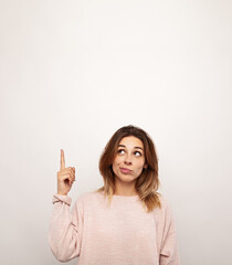 Unsure young woman pointing up against white background