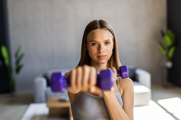 Fototapeta na wymiar Young woman exercising with dumbbells at home. Sporty beautiful woman exercising at home to stay fit.