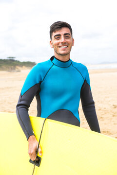Happy young ethnic guy smiling holding surfboard on seashore