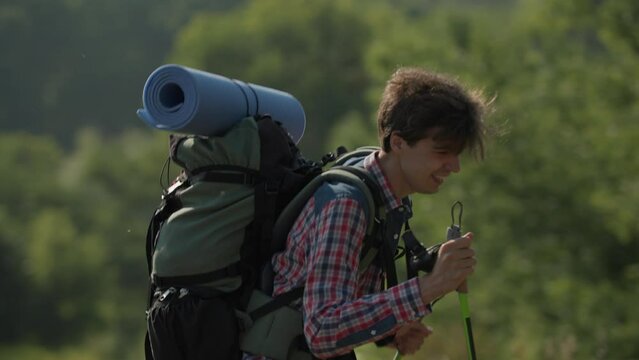Young adult man wearing tourist backpack hiking holding trekking poles.