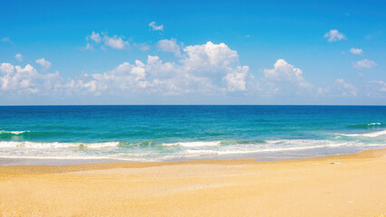 Beautiful background widescreen image of the surf with small caps of white foam, yellowish beach sand and blue sky with clouds.