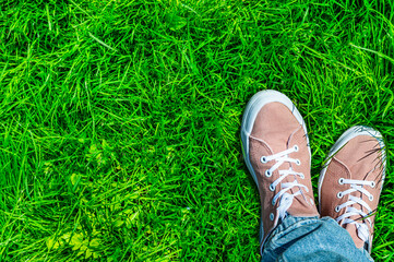 Stylish, trendy bright summer background. Green lawn, nature and human feet. We rejoice in summer, warmth, bright colors. The girl in the park, casual comfortable shoes and clothing style, freedom