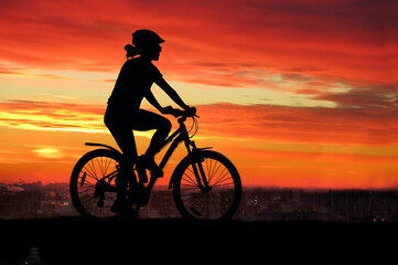 Fototapeta na wymiar Sports, cycling, silhouette of a girl with a sports figure on a bicycle against the background of a colorful bright sunset and the city. Summer landscape, man and nature, transport. Healthy lifestyle,