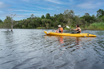 Fototapeta premium Two young Asian tourists go kayaking in a canal through the forest to see natural resources and exercise.