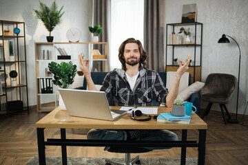 Relaxed caucasian man in casual wear sitting on workplace with modern laptop and meditating with...