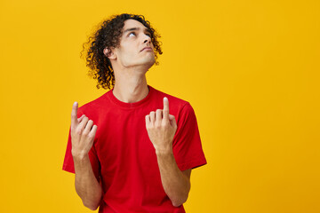 Pensive funny Caucasian young man in red t-shirt point at copy space posing isolated on over yellow studio background. The best offer with free place for advertising. Emotions for everyday concept