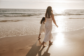 Mother and daughter walking near sea at sunrise