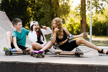 Kids smile and laugh and making selfie on phone together with skateboard and penny boards on the sports ramp playground. Children friendship concept. © Rabizo Anatolii