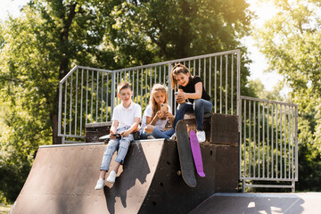 Phone addicted sports children with skateboard and penny boards use phones instead of skating and play together. Children looking at smartphones on sports ramp. Kids addiction of phones.