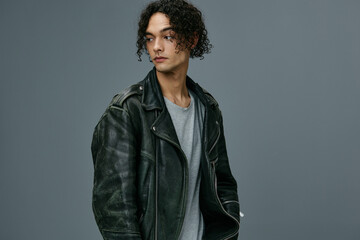 Handsome stylish tanned curly man leather jacket looks aside posing isolated on over gray studio background. Cool fashion offer. Huge Seasonal Sale New Collection concept. Copy space for ad