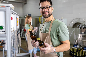 Male brewer working in a brewery filling bottles with beer.
