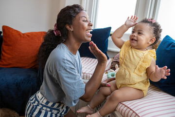 Mother giving baby daughter (12-17 months) high-five at home