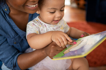 Mother reading to baby daughter (12-17 months) at home - obrazy, fototapety, plakaty