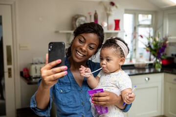Woman using phone and taking care of baby daughter (12-17 months)