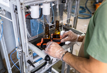 Close up of male brewer hands in a brewery filling bottles with beer.