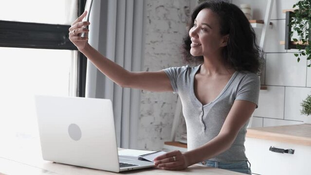 Smiling african american woman taking selfie photos with smartphone while working remotely from home. Joyful person photographing herself with modern touchscreen phone device while doing remote work 