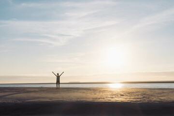 child with arms raised up against the background of the sky,sand on the beach at sunset. Silhouette of a boy at sunset. Beautiful landscape, on the right there is a place for an inscription