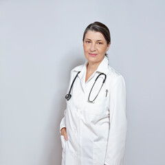 Middle aged female doctor in a white lab coat, smiling friendly, on neutral gray or grey background, copy or text space.