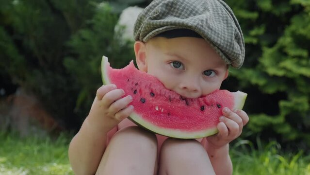 Portrait of cute smiling small boy eating watermelon outdoors. Summer picnic food, childhood concept.