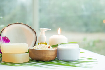 Obraz na płótnie Canvas Coconut oil, tropical leaves and fresh coconuts. Spa coconut products on light wooden background. Spa still life of organic cosmetics with coconuts on a light wooden background, body care concept.
