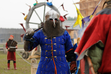 Reenactor man dressed in armor of an Old Rus footman reconstructing swords fight, wooden fortress...