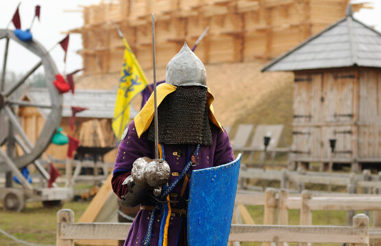 Reenactor man dressed in armor of an Old Rus footman reconstructing swords fight, wooden fortress on a background