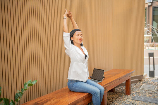 business woman outdoor and laptop,Grinning young woman in white long sleeve shirt stretching in front of desk at home, practicing yoga during break, relieving stress, negative emotions..