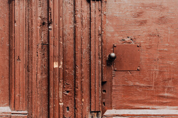 Old home entrance made of a maroon wooden door with scratches and metallic handle