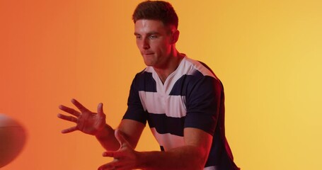 Caucasian male rugby player catching rugby ball over orange lighting