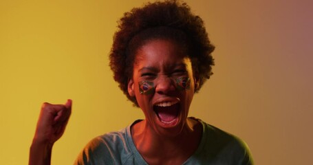 Video of joyful african american female sport fan with flags of portugal on yellow background - Powered by Adobe