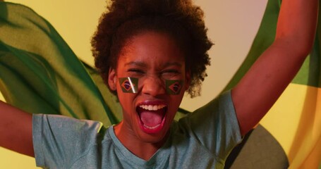 Video of joyful african american female sport fan with flags of portugal on yellow background - Powered by Adobe