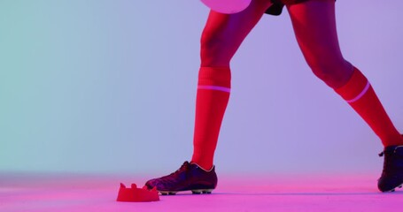 African american female rugby player crouching with rugby ball over neon pink lighting - Powered by Adobe
